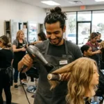 Hair design student in black gloves styling a client's long straight hair at a professional salon in Seattle