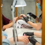 Nail technician wearing protective gloves and mask during chemical nail service following Washington State safety standards