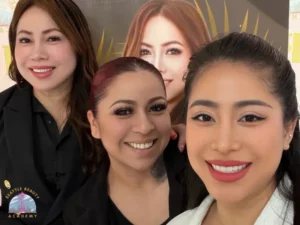Fatima Lalla graduates smile together with her instructors in front of the school banner, one holding a framed Washington State cosmetology license — a moment of shared pride and community
